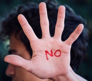Person holding up their hand to the camera with the word "no" written on it.