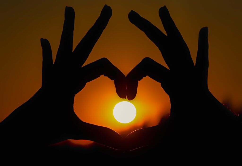 Hands making the shape of a heart with the sun in the middle.