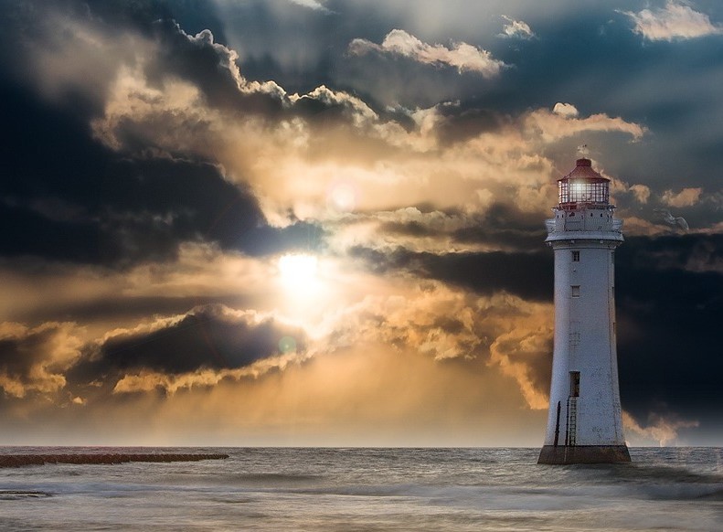 The sun peering through clouds with a lighthouse in the foreground.