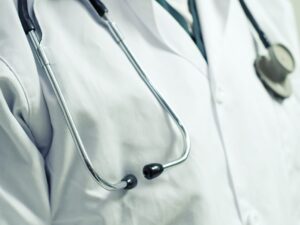 Close up of a stethoscope draped around a doctor's neck wearing a white lab coat.
