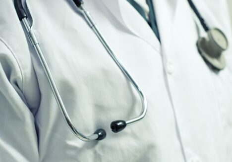 Close up of a stethoscope draped around a doctor's neck wearing a white lab coat.