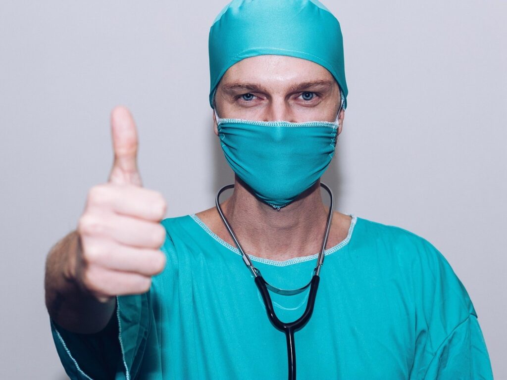 A healthcare worker dressed in scrubs with his thumb up.