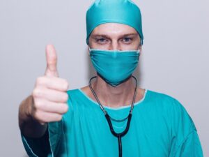 A healthcare worker dressed in scrubs with his thumb up.