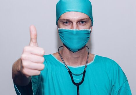 A healthcare worker dressed in scrubs with his thumb up.