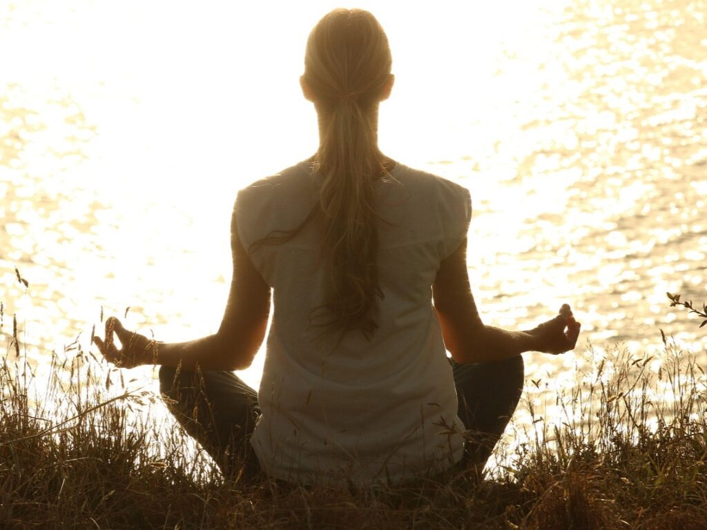 A woman meditating facing a body of water.