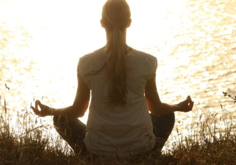 A woman meditating facing a body of water.